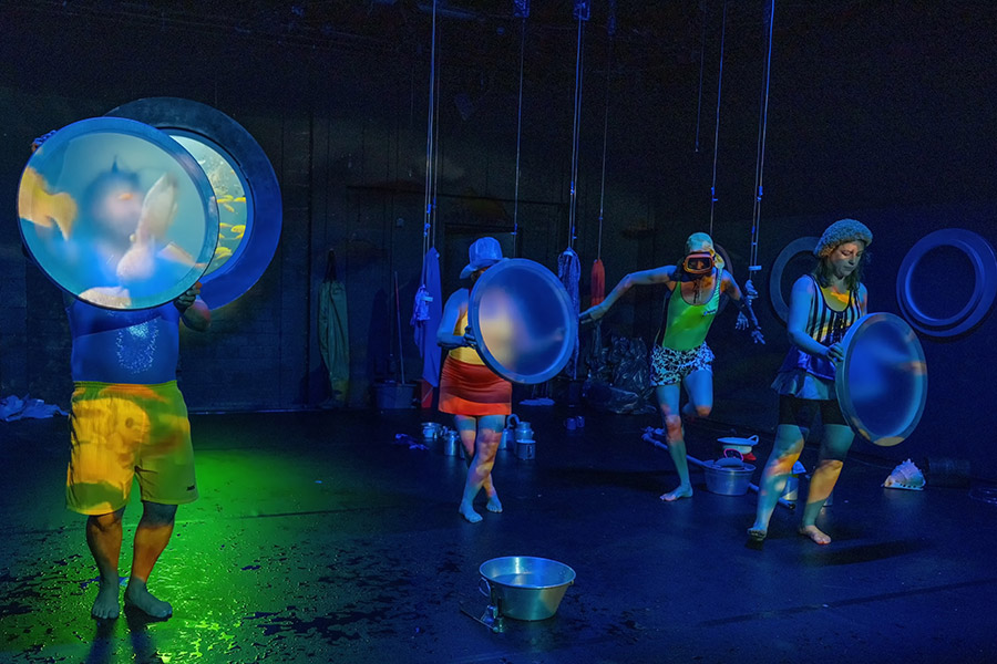 Menschen in Badekleidung auf einer in blaues Licht getauchte Bühne