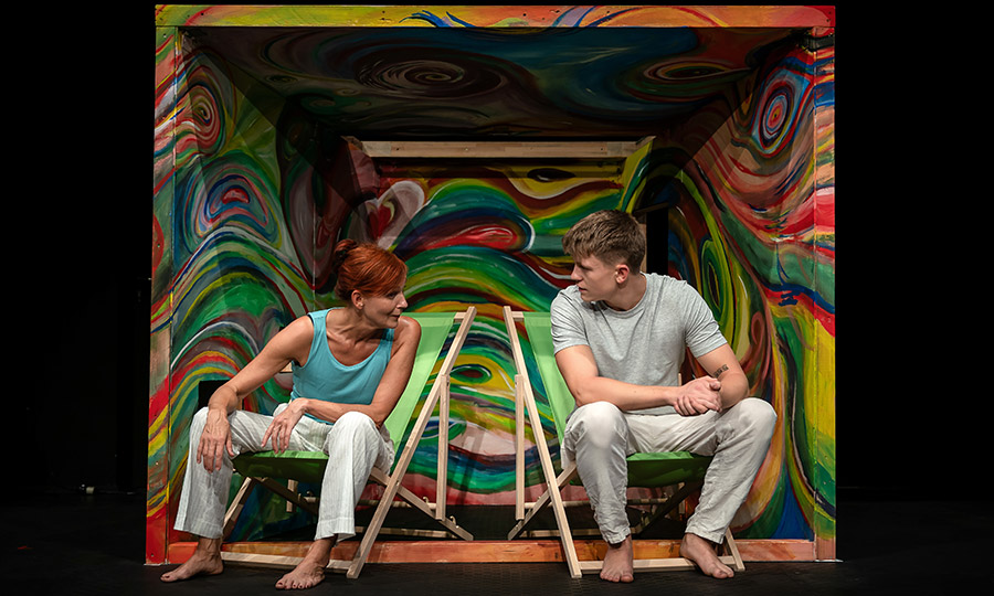 Eine Frau und ein junger Mann sitzen auf Campingstühlen in einem bunt bemalten Verschlag