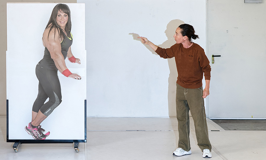 Eine muskulöse Frau auf einer Leinwand, daneben eine Frau, die auf die Leinwand zeigt