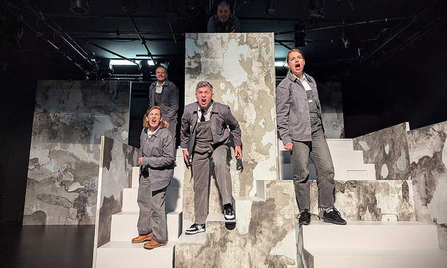 Vier grau gekleidete Personen, die auf einer Treppe stehen und etwas brüllen
