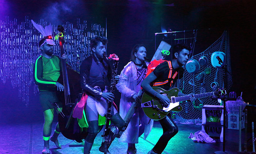 Vier Personen in Taucheranzug und Badekleidung stehen auf einer Bühne und machen Musik