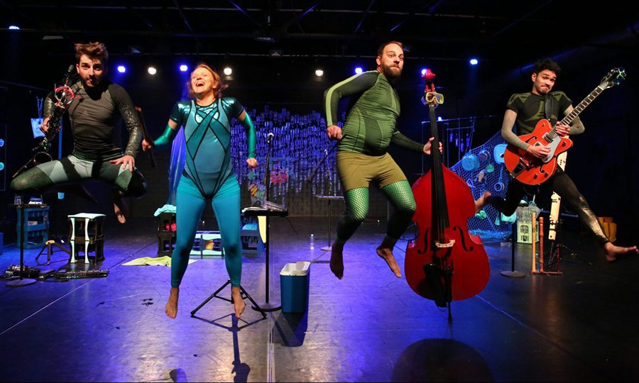 Vier Personen in Badekleidung mit verschiedenen Instrumenten in den Händen springen hoch