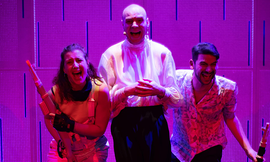 Drei Menschen auf einer lila Bühne schreien verängstigt