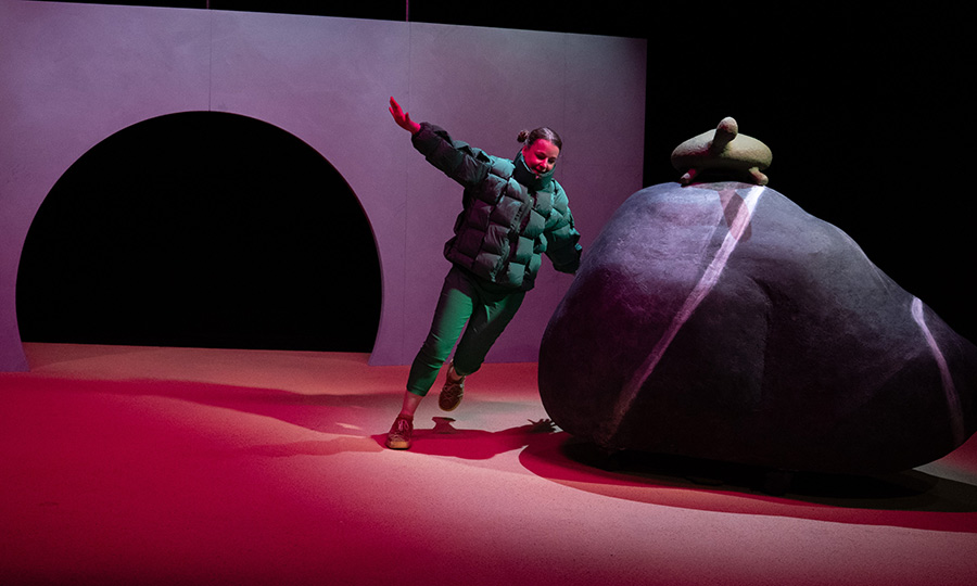 Eine Person rennt um einen großen Felsen herum, auf dem eine Schildkröte aus Pappmaché sitzt.