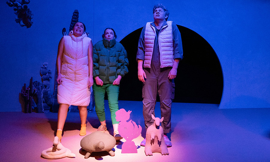 Drei Personen gucken erschrocken nach oben. Zu ihren Füßen stehen Pappmaché-Figuren: eine Schlange, eine Schildkröte, und ein Gürteltier.