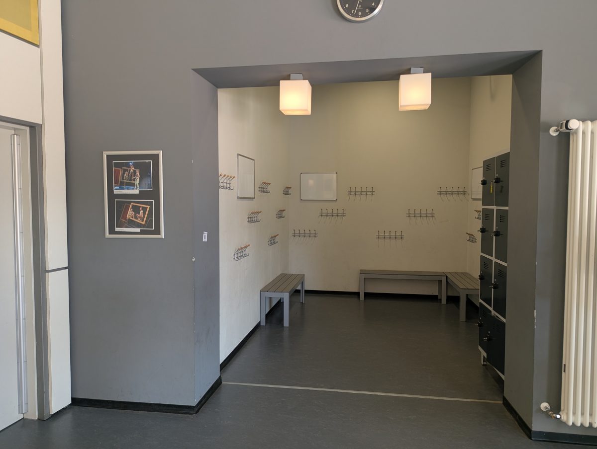 Die Garderobe des überzwerg – Theater am Kästnerplatz: Ein offener Raum mit Haken in verschiedenen Höhen, Bänken und Spinden zum Verschließen von Wertsachen.